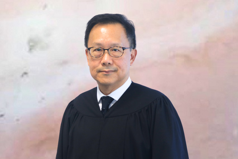 Man in judicial robe and glasses against mottled background.